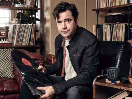 HD desktop wallpaper featuring a man from Loudermilk holding a vinyl record, surrounded by a cozy, music-themed interior.