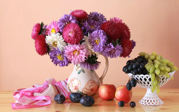 A vibrant still life HD wallpaper featuring a flower-filled vase alongside fresh fruit arranged on a wooden table against a soft peach background.