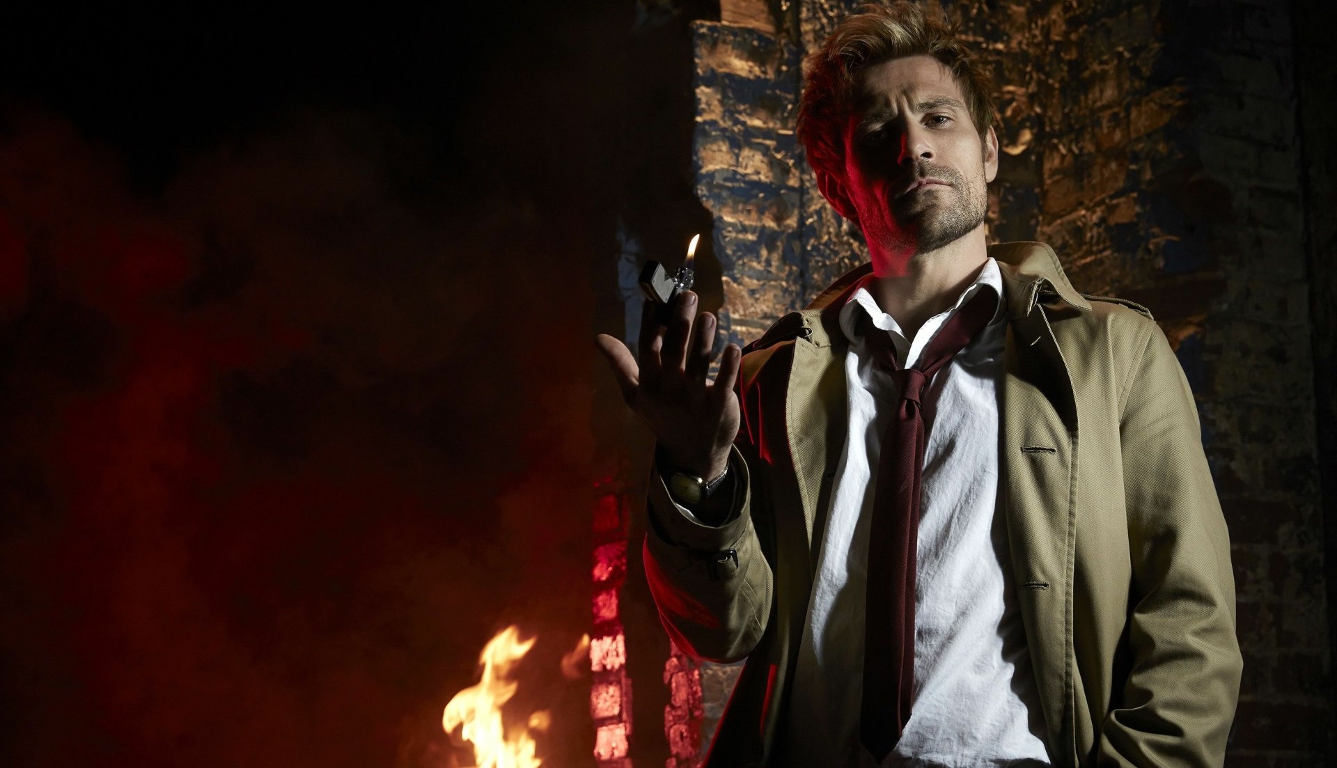 John Constantine from Constantine (TV show) in a trench coat amid flames and crumbling stone — 2K Quad HD PC desktop wallpaper/background.