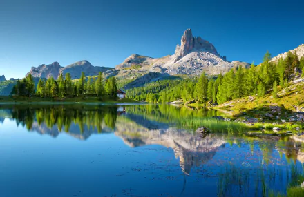 HD landscape wallpaper showcasing a serene mountain in Italy, its peak and surrounding trees beautifully reflected in a clear lake under a bright blue sky.