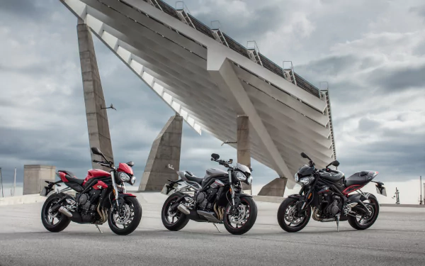 Three Triumph Street Triple motorcycles (vehicles) parked beneath an angular concrete structure, high-detail 4K Ultra HD PC desktop wallpaper background.