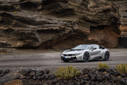 Silver BMW i8 supercar parked on a rugged road with rocky cliffs in the background, captured in stunning 4K Ultra HD as a PC desktop wallpaper.