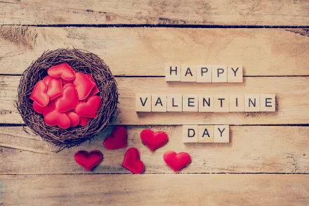 Romantic HD desktop wallpaper featuring a nest filled with heart-shaped objects and scrabble tiles spelling Happy Valentine's Day on a wooden background, celebrating love and the holiday.