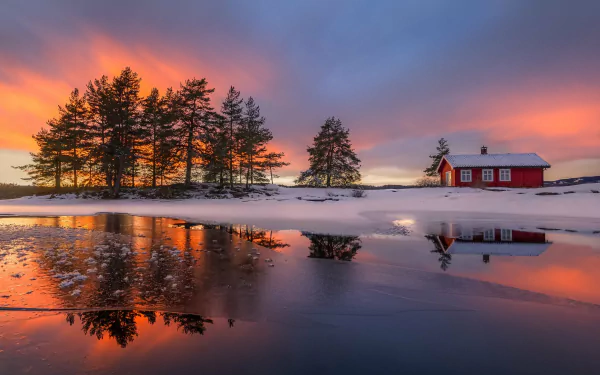 HD desktop wallpaper featuring a winter scene with a house near a frozen lake, snow-covered ground, trees, and a stunning sunset reflecting on the icy water.
