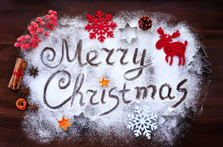 A festive Merry Christmas message written in powdered sugar on a wooden surface, surrounded by holiday decorations like red berries, cinnamon sticks, and snowflakes.