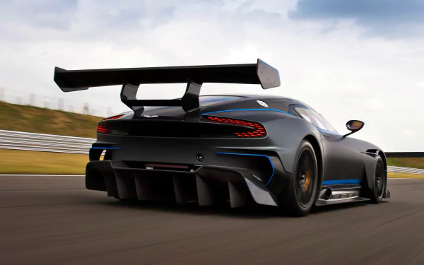 Rear three-quarter view of a matte black Aston Martin Vulcan supercar speeding on a racetrack — HD PC desktop wallpaper background.