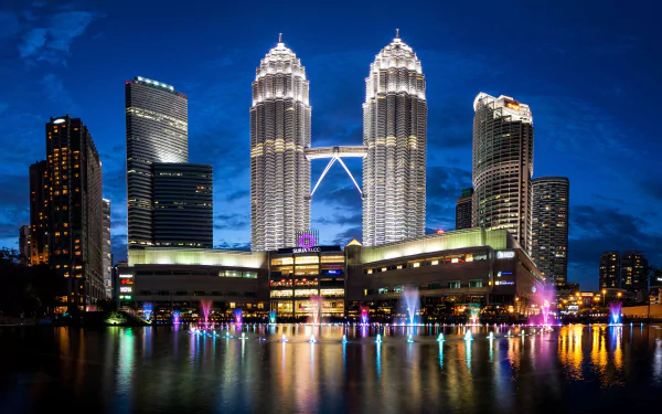 Night view of Kuala Lumpur skyline featuring the illuminated Petronas Towers and surrounding skyscrapers, reflected on the water, captured in 4K Ultra HD.
