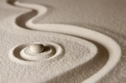 Close-up 4K Ultra HD wallpaper of a smooth stone resting on sand with Zen-inspired, flowing carved lines, evoking calm and religious tranquility.