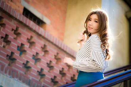 4K Ultra HD PC desktop wallpaper of a brunette woman model smiling on stairs, shallow depth of field with soft sunlight and a brick background.
