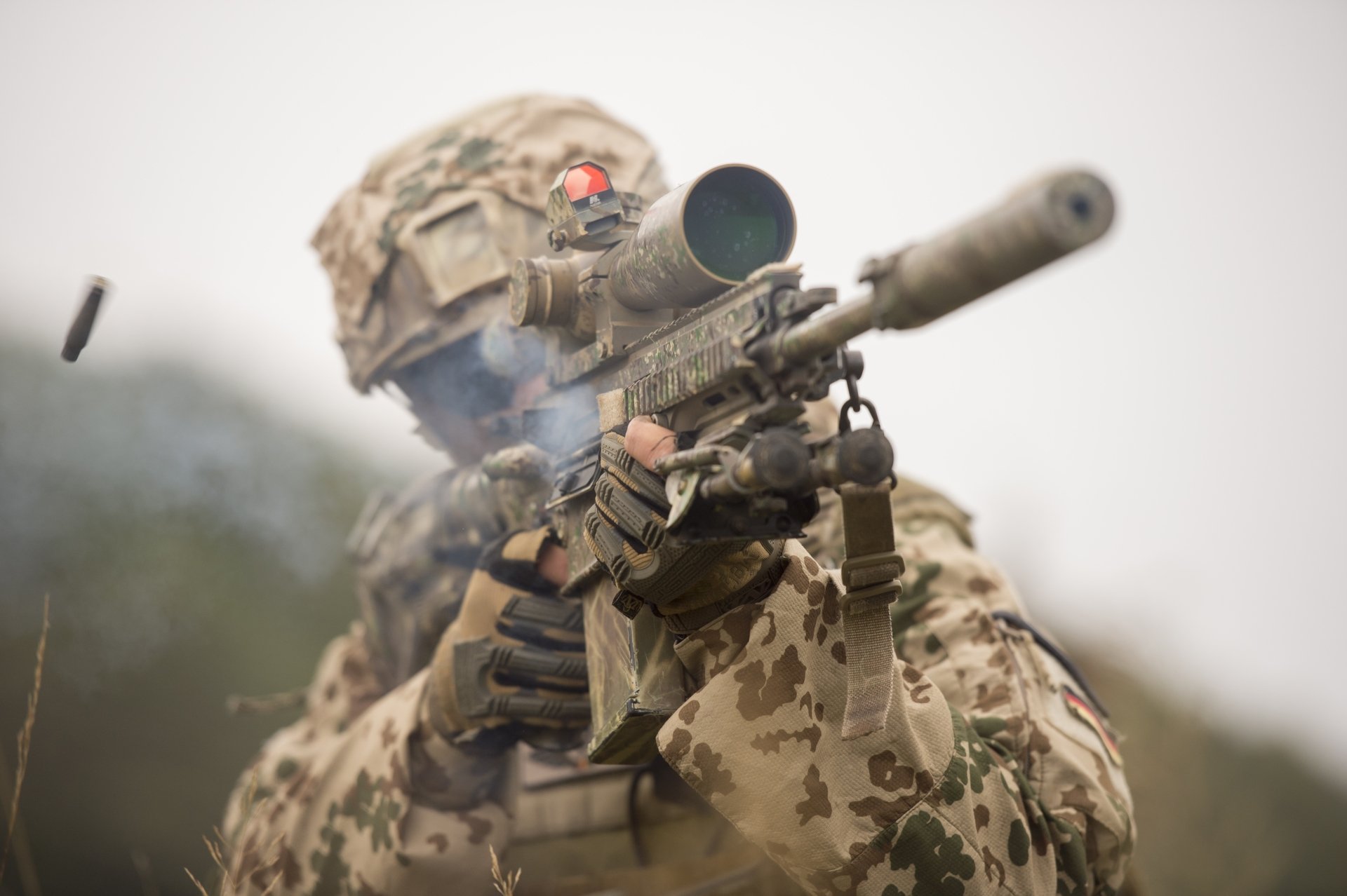4K Ultra HD desktop wallpaper of a soldier in camouflage firing a military assault rifle, with a shell casing ejecting mid-air.