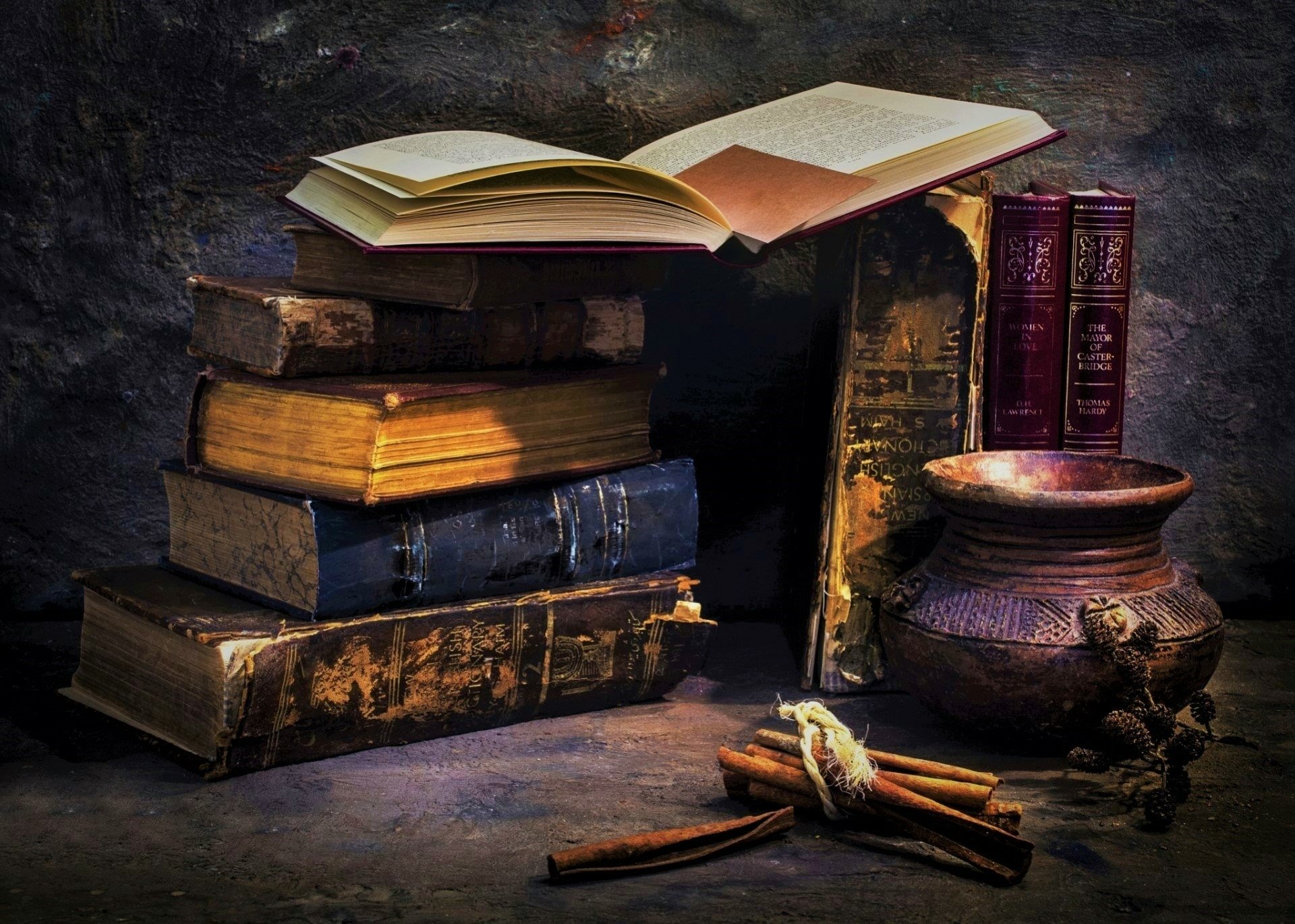 A still life HD desktop wallpaper featuring stacked antique books, an open book, a rustic vase, a bowl, and tied cinnamon sticks arranged artistically.