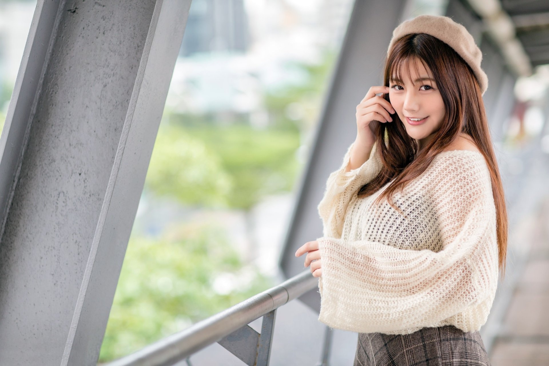 An HD desktop wallpaper featuring a smiling Asian woman with long brunette hair and brown eyes, wearing a hat and a cozy sweater. The image has a depth of field effect, creating a soft, blurred background.