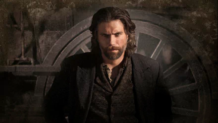 HD PC desktop wallpaper of a brooding bearded man in a period coat set before a large iron wheel, from the TV show Hell on Wheels.