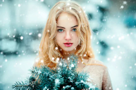 Blonde woman with blue eyes and lipstick holds frosted pine branches amid softly falling snow, captured in a HD depth of field portrait for a desktop wallpaper background.