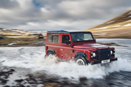 A Land Rover Defender splashes through a river in an off-road adventure, captured with motion blur, set against a dynamic HD background.