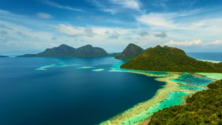 Aerial view of Dulang Island, Malaysia, surrounded by turquoise ocean waters and lush greenery under a bright blue sky, showcasing stunning natural beauty.