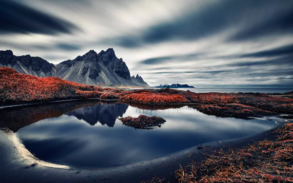 HD desktop wallpaper featuring Vestrahorn in Iceland with a stunning reflection on a calm body of water, capturing the serene horizon, rugged mountain peaks, and dramatic clouds over the tranquil ocean.