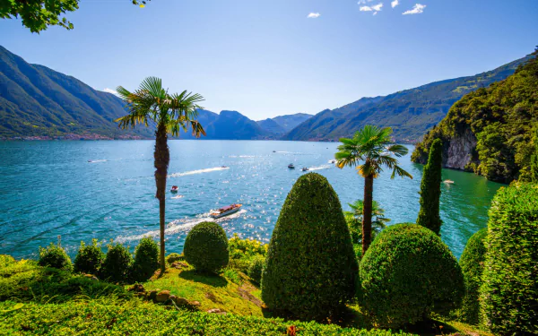 HD desktop wallpaper featuring a vibrant photograph of Lake Como, Italy, with lush trees and greenery framing the serene blue lake and surrounding mountains.