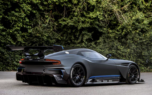 Aston Martin Vulcan supercar race car in dark grey, showcased on a road with lush green foliage in the background, captured as a 4K Ultra HD PC desktop wallpaper.