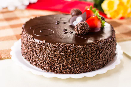 HD desktop wallpaper featuring a delicious chocolate cake adorned with strawberries and chocolate garnish, showcasing a rich, glossy finish and chocolate sprinkles, surrounded by a checkered tablecloth and flowers.