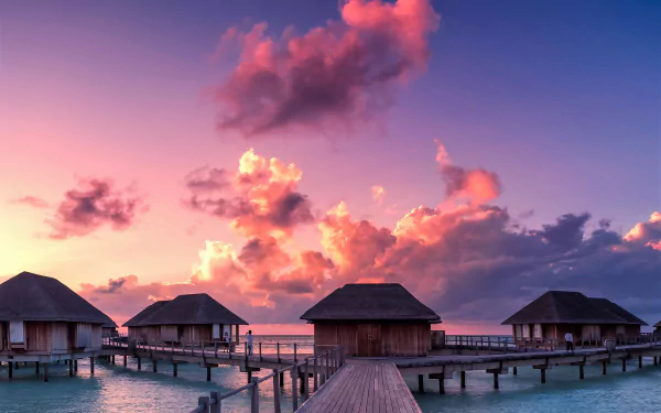 Overwater bungalows at a Maldives resort stretch over the calm ocean, set against a vibrant sunset sky, captured in HD for a serene desktop wallpaper.