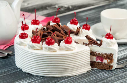 HD desktop wallpaper of a cream-covered cherry cake with chocolate shavings, decorated with whole cherries and served alongside white cups and a teapot.