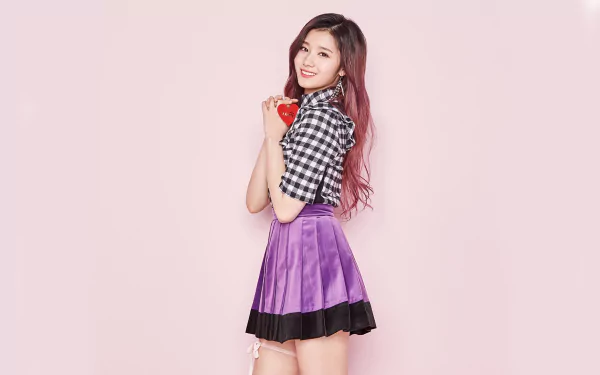 A smiling Korean K-pop singer from Twice with long red hair, brown eyes, wearing a checkered top and purple skirt, posing against a light pink background.
