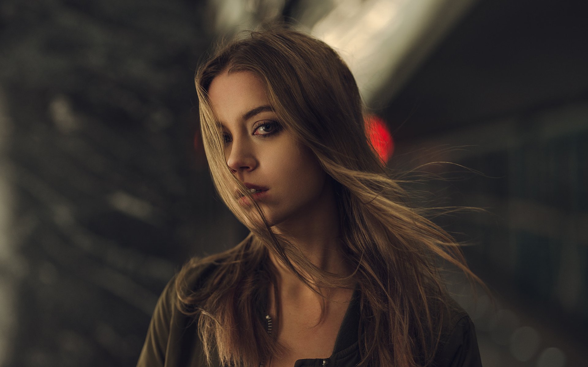 HD PC desktop wallpaper of a blonde model woman with long hair and brown eyes, wind-tossed hair against a moody urban night background.