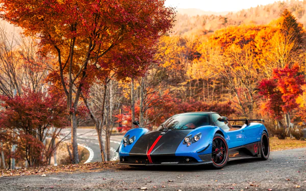 A blue Pagani Zonda supercar parked on a winding road surrounded by vibrant autumn trees in a 4K Ultra HD desktop wallpaper.