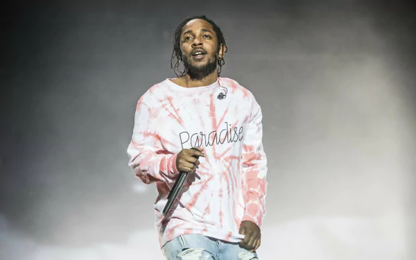 Kendrick Lamar performing live, wearing a pink tie-dye sweatshirt and holding a microphone, captured in high definition. A vibrant background for music enthusiasts.