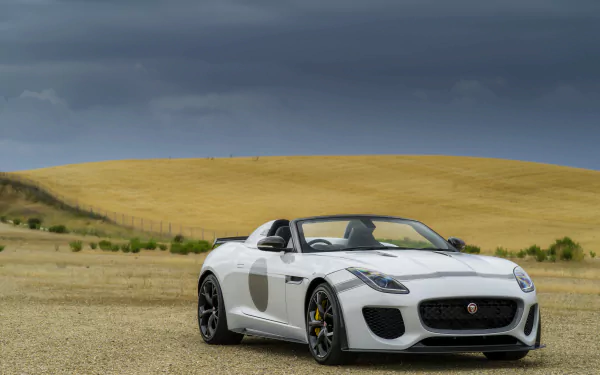 White Jaguar F-Type convertible on a gravel plain with rolling golden hills under a dramatic sky — 5K Ultra HD PC desktop wallpaper and background of the sports car.