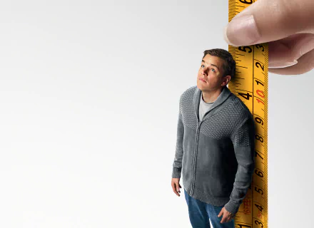 HD desktop wallpaper featuring a character from Downsizing next to a giant measuring tape, highlighting the movie's miniature theme.