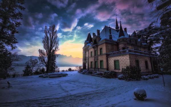 Hunegg Castle in Switzerland at dusk with a dramatic sunset sky, surrounded by snow-covered ground and silhouetted trees. 4K Ultra HD desktop wallpaper.