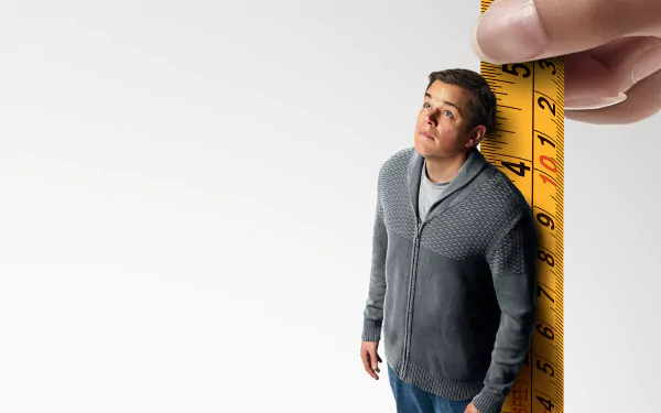 HD desktop wallpaper featuring a character from Downsizing next to a giant measuring tape, highlighting the movie's miniature theme.