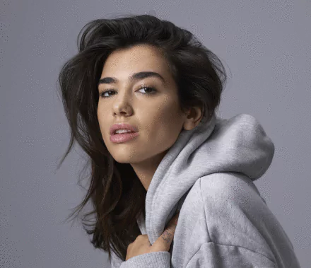 HD PC desktop wallpaper featuring a close-up portrait of Dua Lipa wearing a gray hoodie, highlighting her confident expression in a music-themed setting.