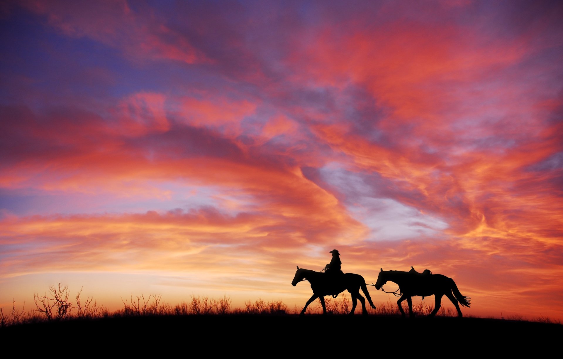 Silhouette of a cowboy riding a horse against a vibrant sunset sky with dramatic clouds. HD desktop wallpaper and background featuring sky, cloud, silhouette, horse, and sunset photography.