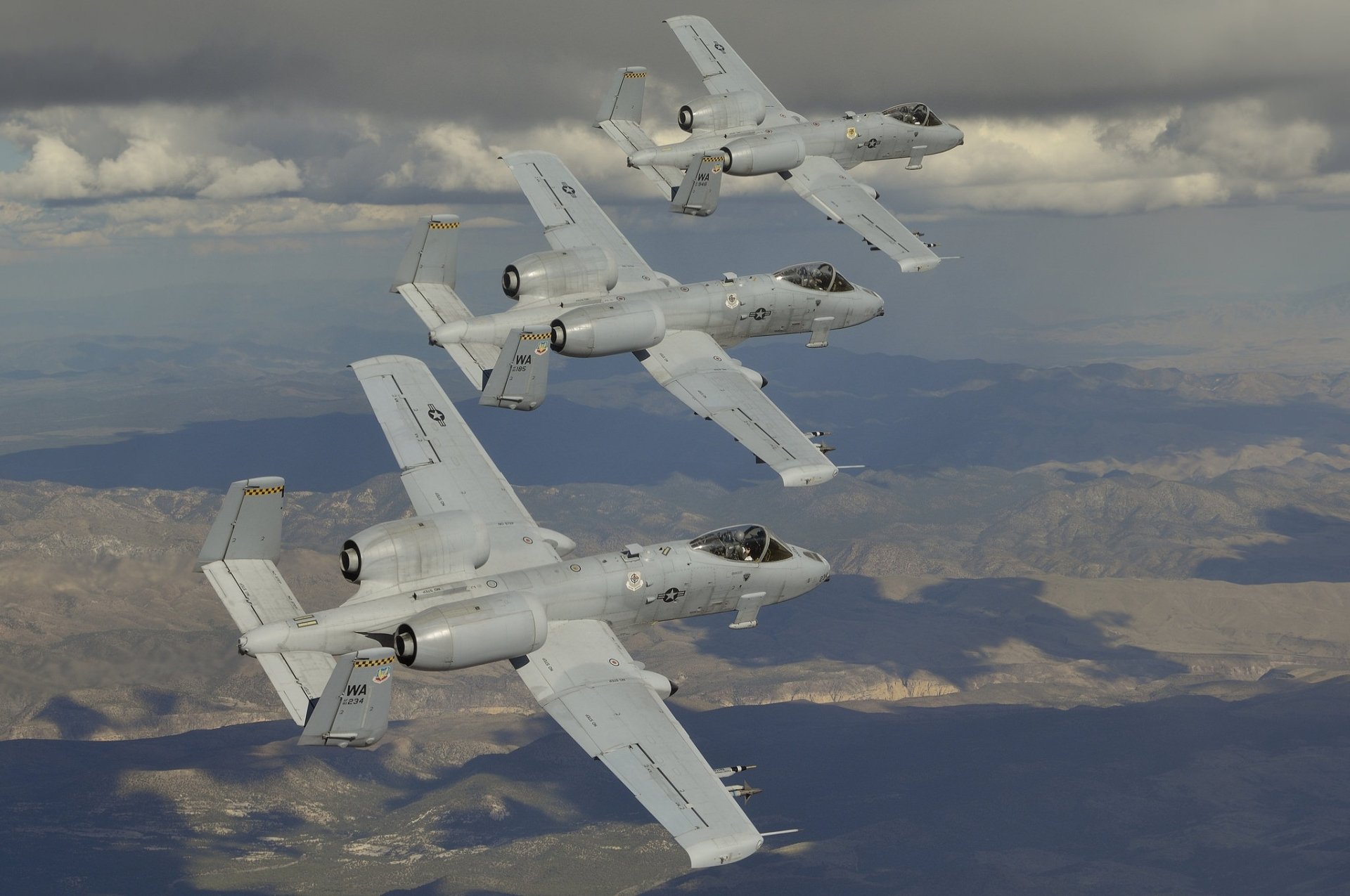 Three Fairchild Republic A-10 Thunderbolt II jet fighter warplanes fly in formation over a mountainous landscape, displayed in a high-definition desktop wallpaper.