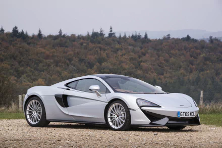 Silver McLaren 570GT supercar parked on gravel with forested hills — 4K Ultra HD PC desktop wallpaper and background showcasing the sleek silver car/vehicle.