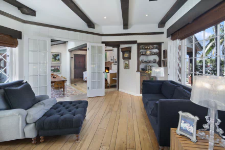 A bright living room with wooden floors, exposed ceiling beams, and modern sofas arranged around a cozy, inviting space, captured in 4K Ultra HD quality.