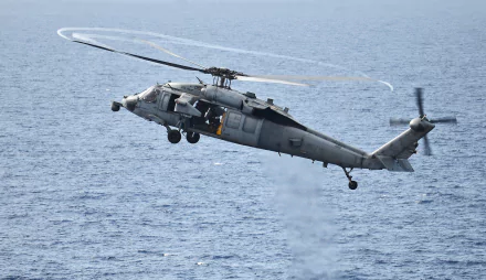 HD desktop wallpaper showing a military Sikorsky SH-60 Seahawk helicopter aircraft banking over the ocean with rotor wake visible.