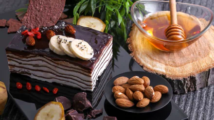 HD desktop wallpaper featuring a layered chocolate almond cake topped with banana slices, accompanied by honey, whole almonds, and chocolate pieces in a still life dessert setting.