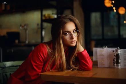 HD desktop wallpaper of a blonde, long-haired woman model wearing glasses, leaning on a cafe table; shallow depth of field with warm bokeh lights.