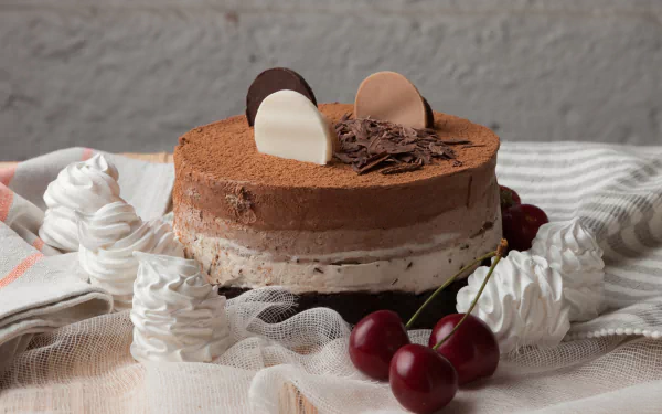 HD desktop wallpaper showcasing a chocolate cake dessert adorned with cherries, meringue swirls, and chocolate decorations on a soft fabric background.