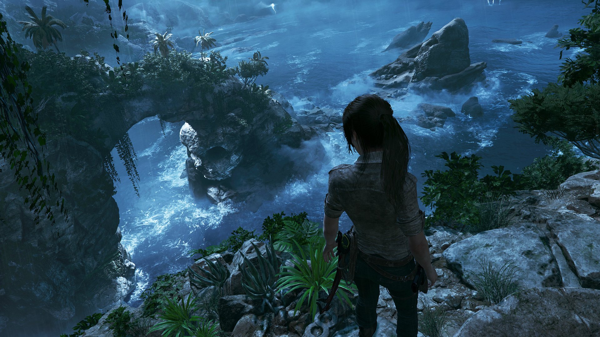 HD desktop wallpaper featuring Lara Croft from the video game Shadow of the Tomb Raider, gazing over a lush landscape with rocky formations and water below.