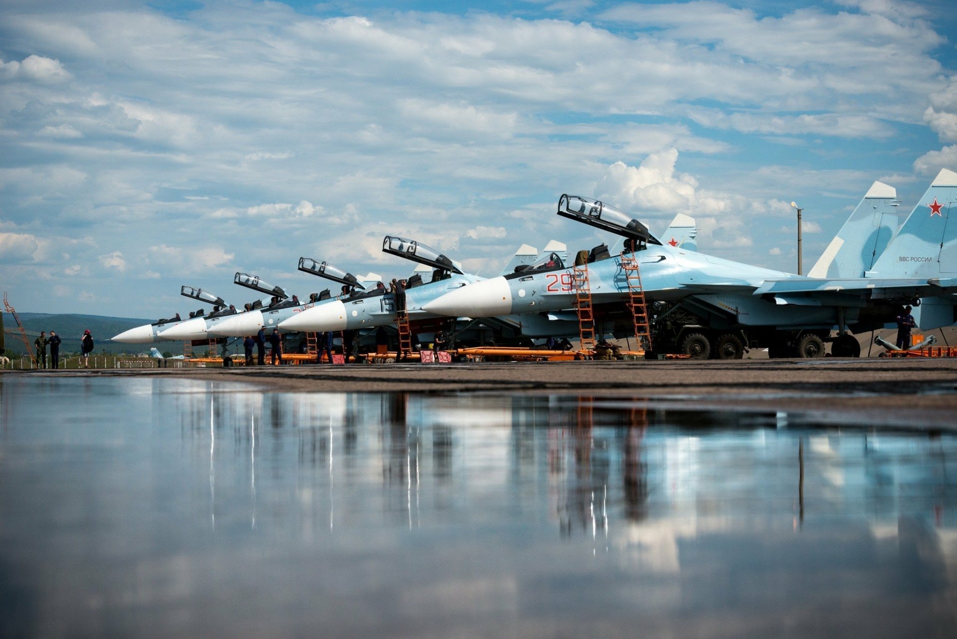 A reflection of multiple Sukhoi Su-30 jet fighters lined up on a tarmac under a partly cloudy sky, captured as an HD desktop wallpaper and background.