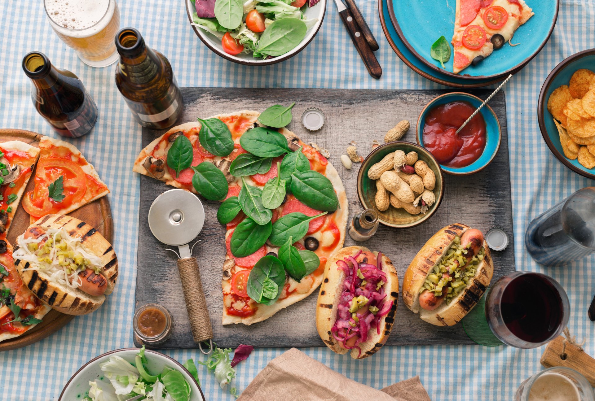5K Ultra HD PC desktop wallpaper and background: food still life of pizza with basil, two hot dogs with toppings, bowls of chips, sauces and drinks on a checkered table.