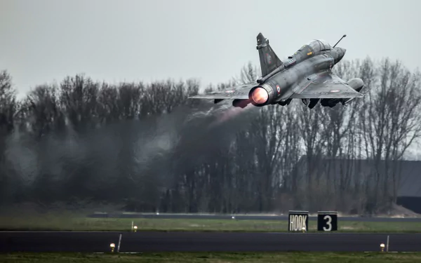 Dassault Mirage 2000 military jet fighter warplane climbing from runway with afterburner and exhaust trail against a tree-lined sky — 2K Quad HD PC desktop wallpaper.