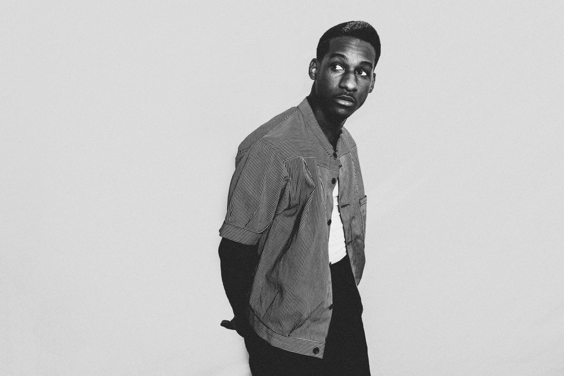 A black and white HD wallpaper featuring Leon Bridges, showcasing his stylish outfit and contemplative pose, capturing the essence of music and artistry.