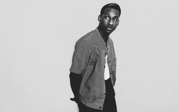 A black and white HD wallpaper featuring Leon Bridges, showcasing his stylish outfit and contemplative pose, capturing the essence of music and artistry.