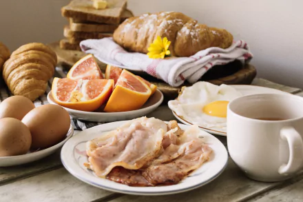 2K Quad HD PC desktop wallpaper/background showing a breakfast spread: croissant, bacon, fried egg, grapefruit wedges, whole eggs, sliced bread and a coffee cup on a tablecloth.